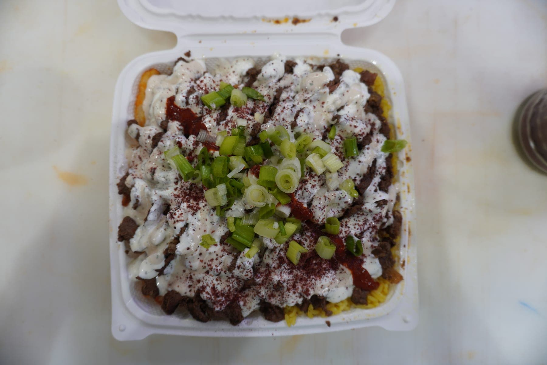 A beef bowl over saffron rice under garlic sauce, hot sauce, sumac and green onion