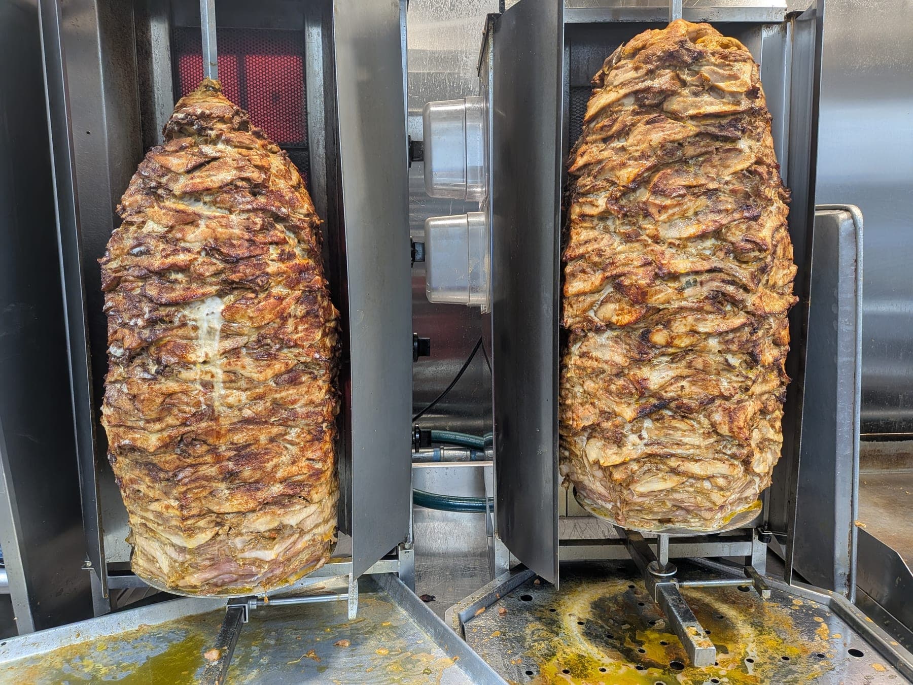 Two shawarma spits turning against the broiler, crusted brown down the outside