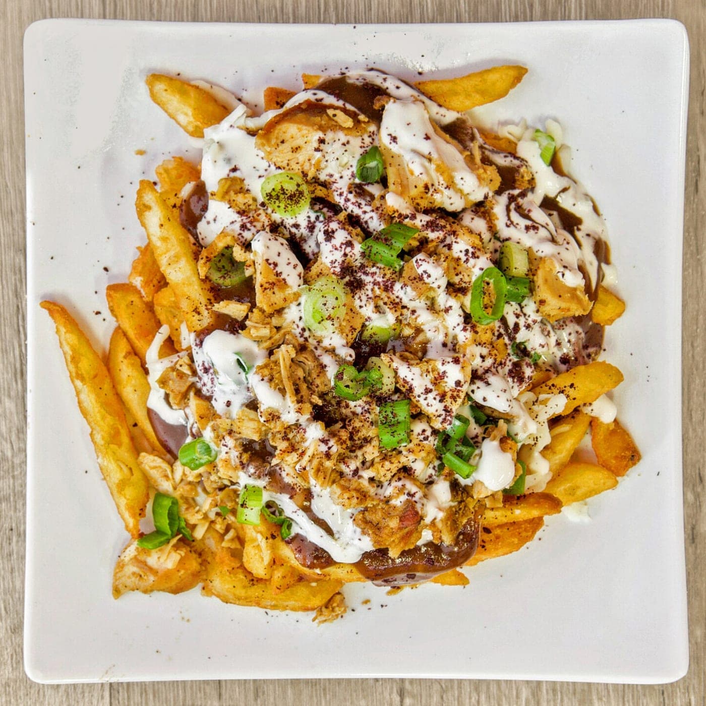 A plate of fries under shawarma, garlic sauce, sumac and green onion