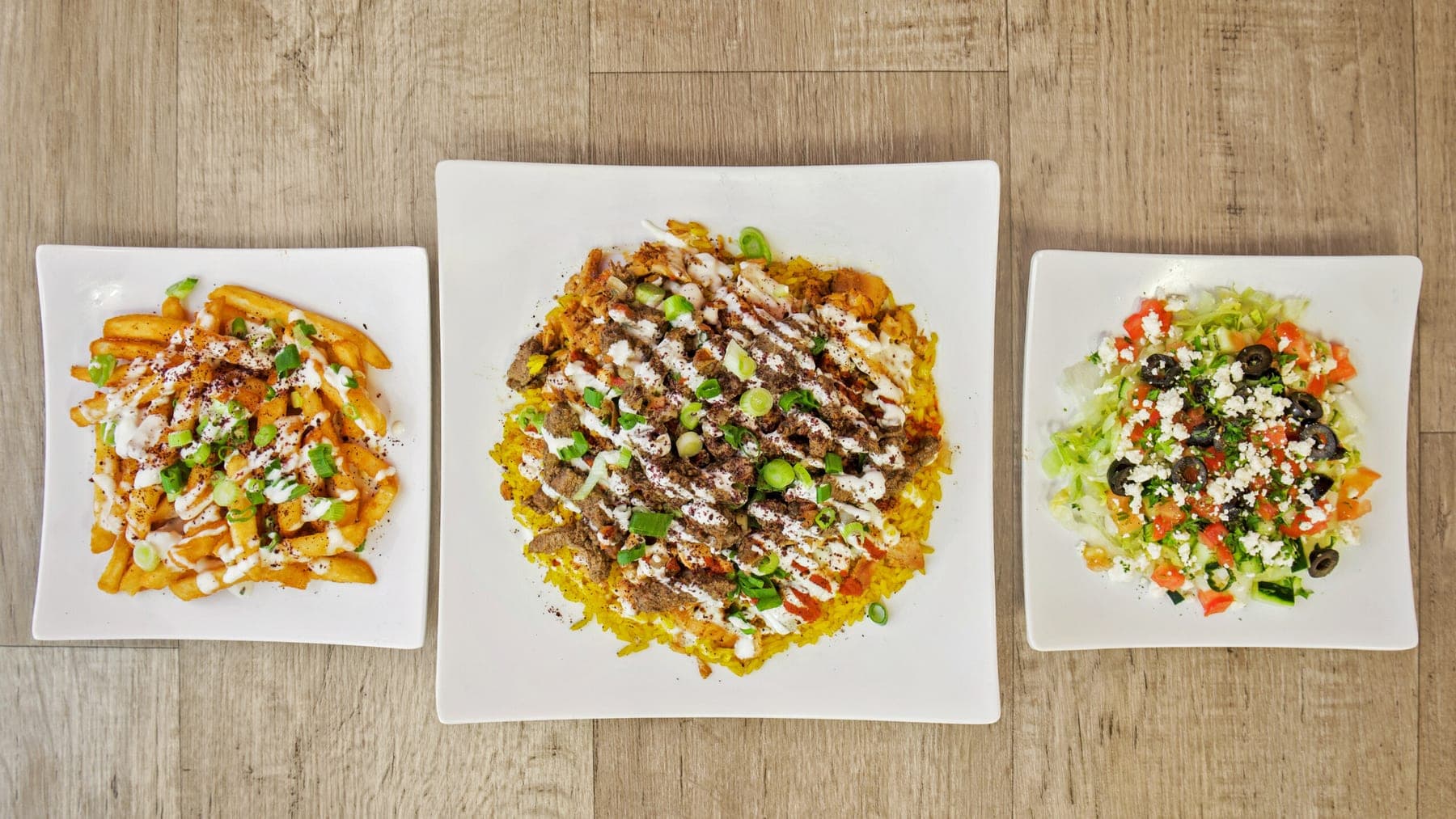Three plates of shawarma over saffron rice, dressed with garlic sauce and green onion