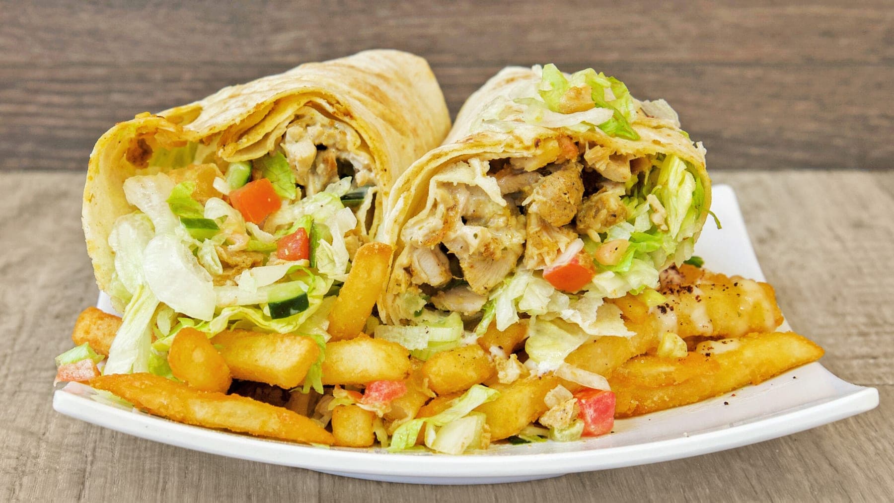 A shawarma wrap cut in half, standing over a tray of loaded fries